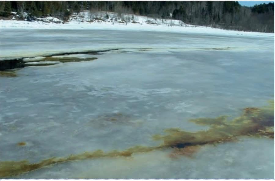 La photo montre un lac gelé avec une crevasse au centre et une émersion d’hydrocarbures à la surface de la glace. Crédit photo : Un guide pratique d’interventions sur les rives en eau douce : chapitre 4, Environnement et Ressources naturelles, Gouvernement du Canada. La reproduction est une copie de la version disponible au https://www.canada.ca/fr/environnement-changement-climatique/services/eau-apercu/proteger-eau-douce/guide-pratique-interventions-sur-rives-eau-douce/chapitre-4.html#toc10.