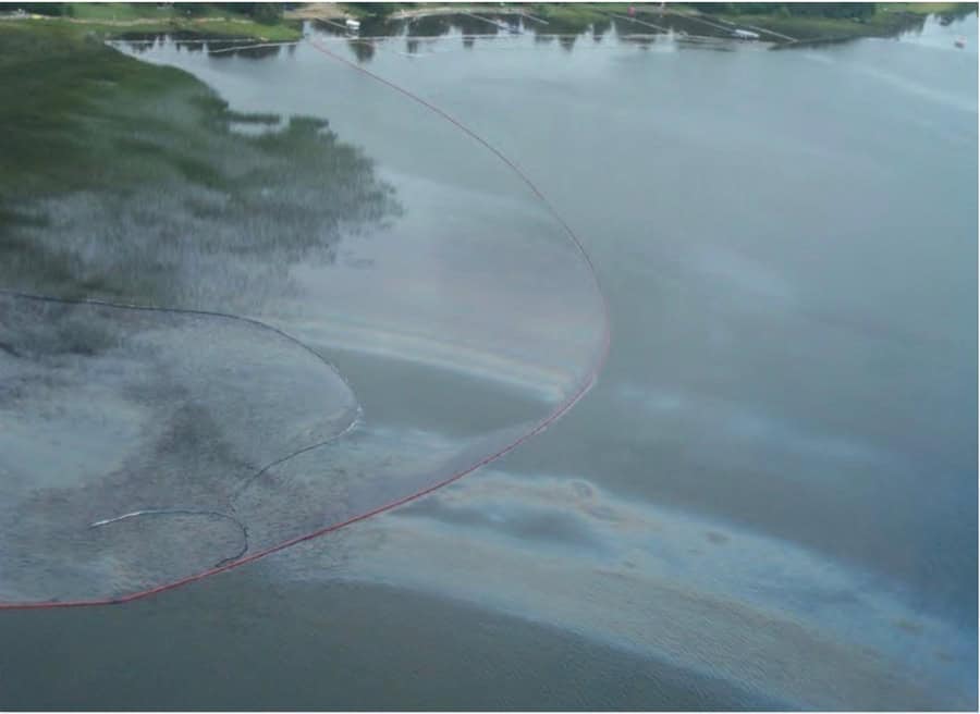 Figure 4.2 : La photo montre un reflet d’huile fragmenté sur la surface de l’eau du lac Wabamun (AB) avec une installation de barrages flottants retenant l’huile. Crédit photo : Un guide pratique d’interventions sur les rives en eau douce : chapitre 4, Environnement et Ressources naturelles, Gouvernement du Canada. La reproduction est une copie de la version disponible au https://www.canada.ca/fr/environnement-changement-climatique/services/eau-apercu/proteger-eau-douce/guide-pratique-interventions-sur-rives-eau-douce/chapitre-4.html#toc10.